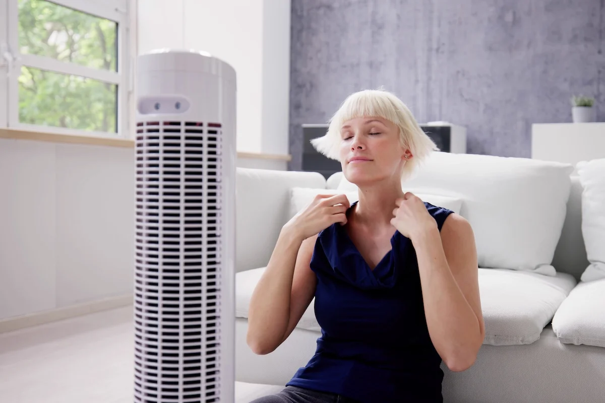 Young Woman Cooling Herself In Front Of Bladeless Tower Fan At Home