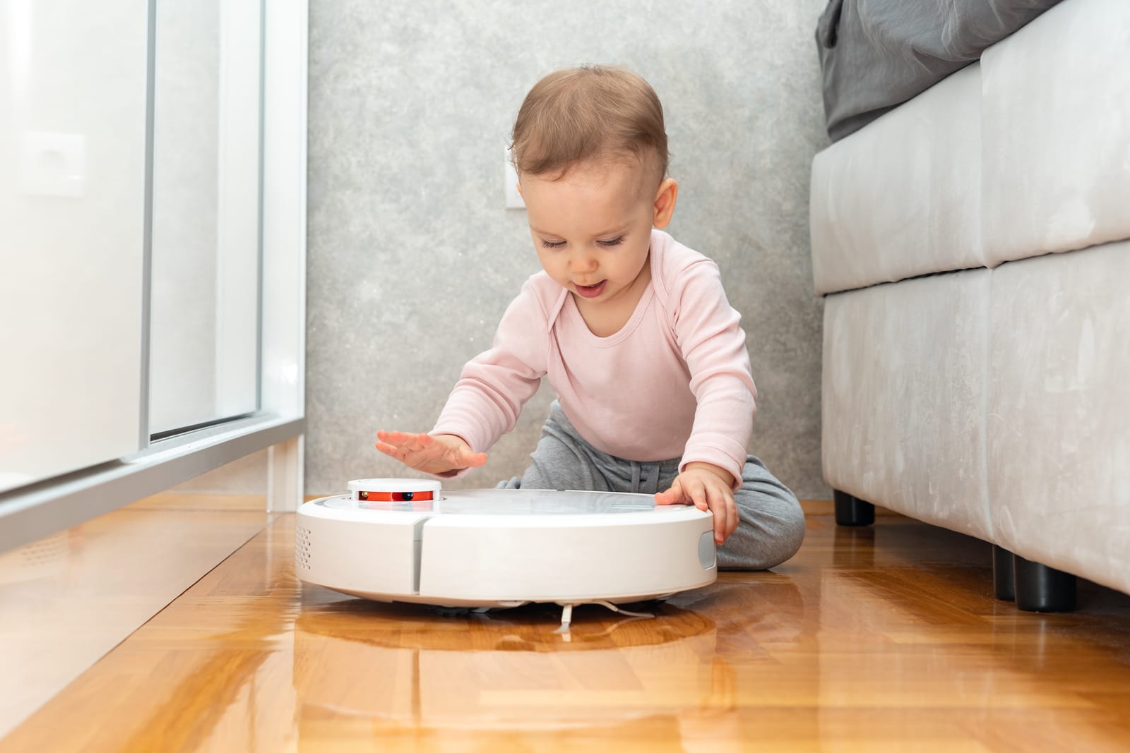 a baby slaps his palm on the surface of a robot vacuum cleaner