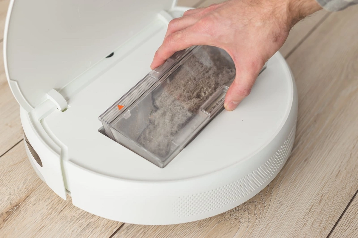 the hand pulls out a container of garbage from the robot vacuum cleaner