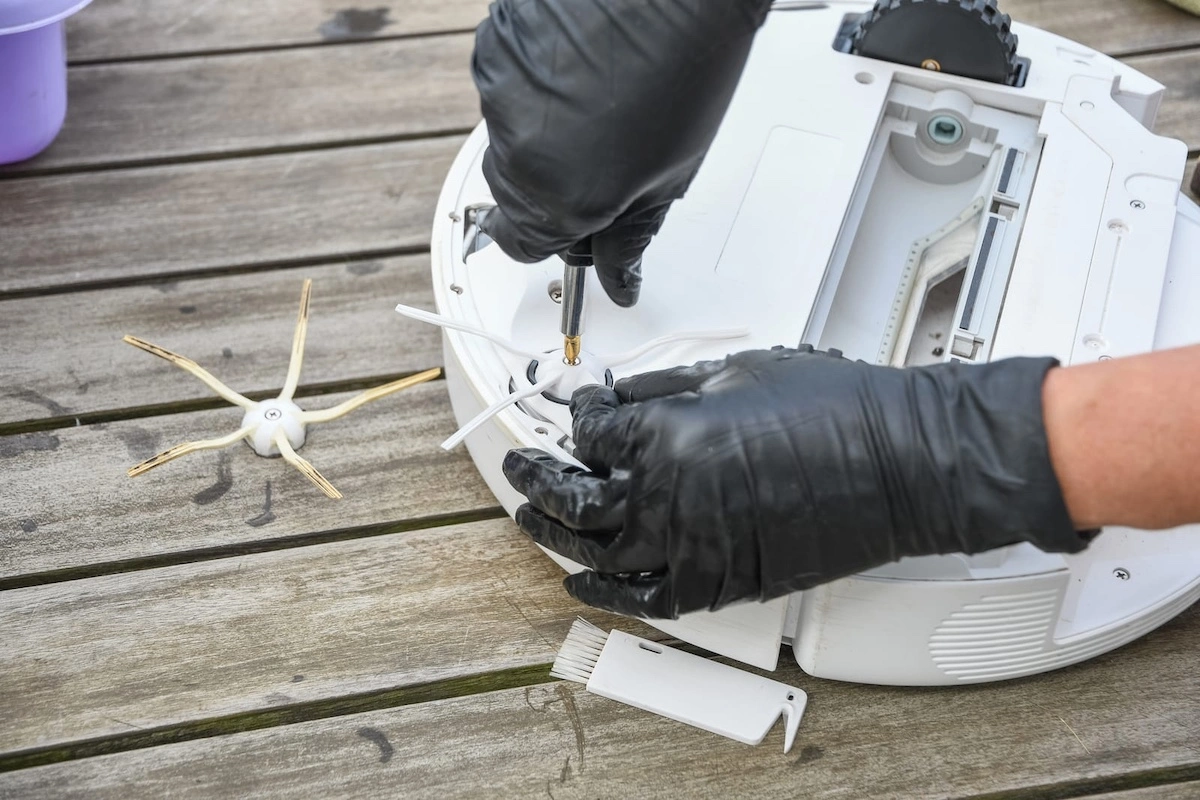 a woman unscrews the side brush from a robot vacuum cleaner with a screwdriver