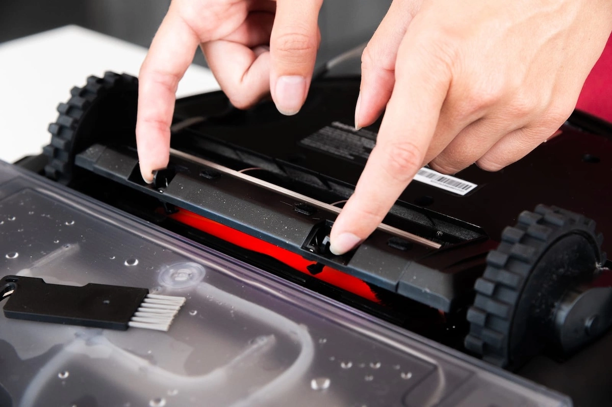 close up of a young caucasian womans hands servicing the brush compartment of a robot vacuum cleaner automated home cleaning systems