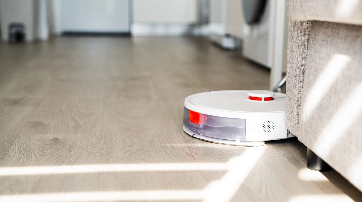  robot vacuum cleaner cleaning wooden floor under sofa in modern apartment